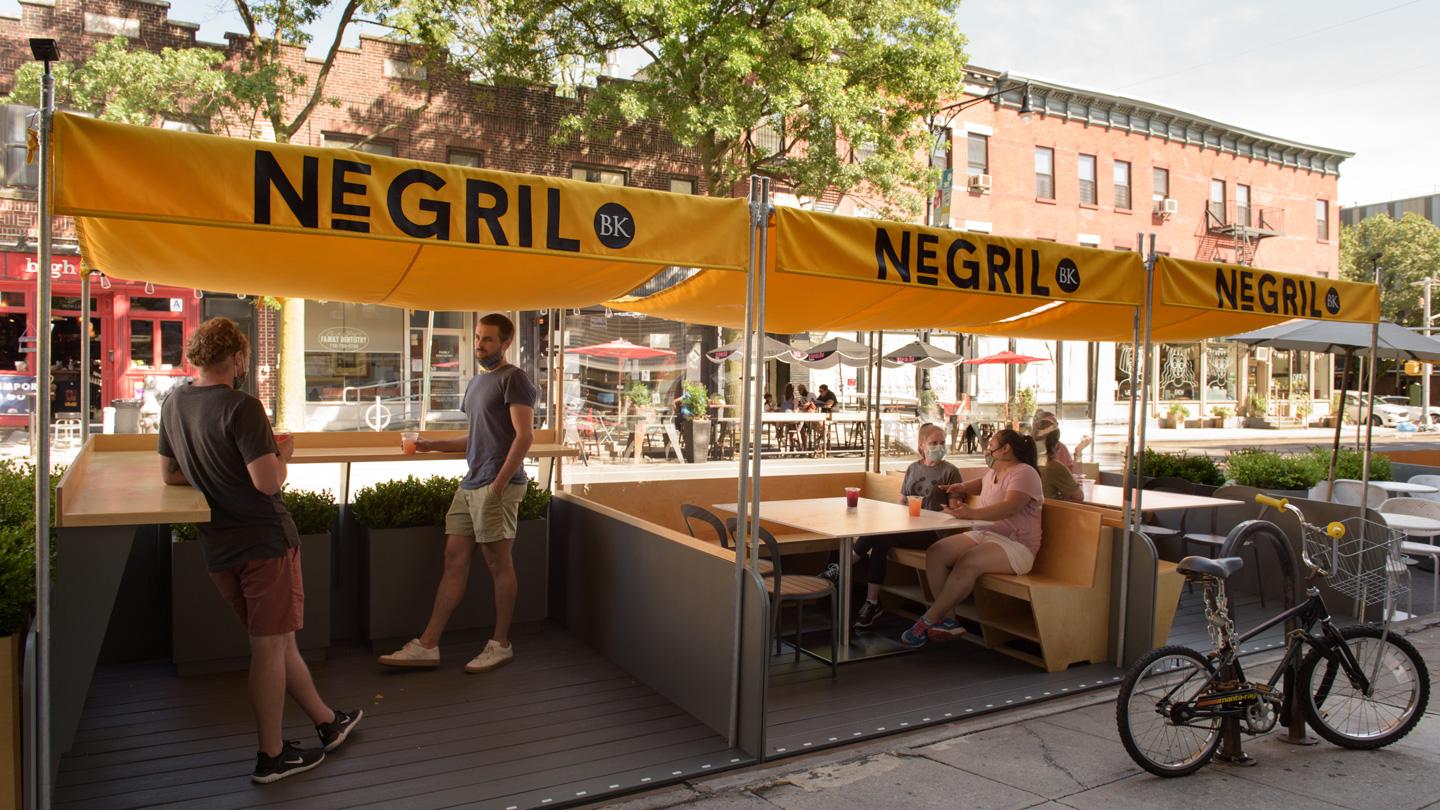 Four people hanging out in DineOut pavilions outside of Negril restaurant in Brooklyn