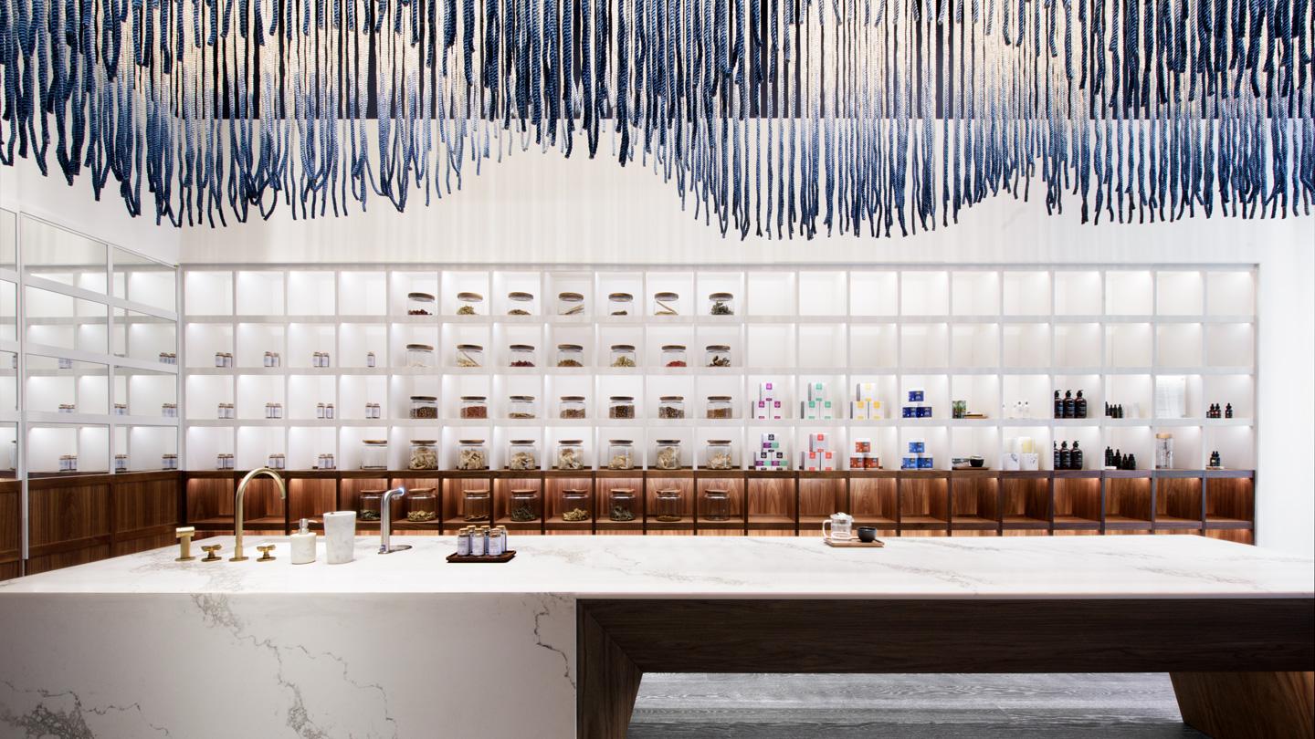 Shelving behind a a dip-dyed rope installation above a reception counter inside ORA 