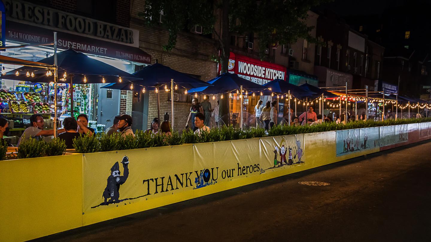 Night time view of murals and people dining outside at DineOut Elmhurst designed by Rockwell Group