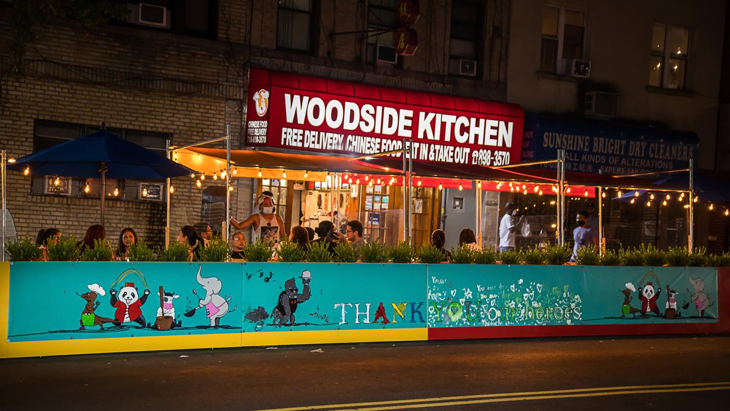 Night time view of murals and open street dining at DineOut Elmhurst designed by Rockwell Group