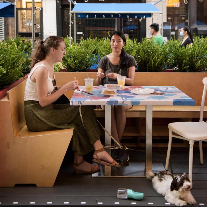 Two women with a dog eating in dining booth DineOut Mott Street designed by Rockwell Group