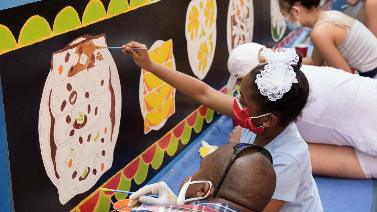 Children and a parent painting a mural of dim sum at DineOut Mott Street designed by Rockwell Group