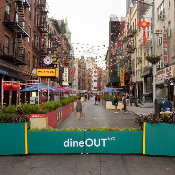 View looking down open street Mott Street with DineOut outdoor dining pavilions in parking spaces.